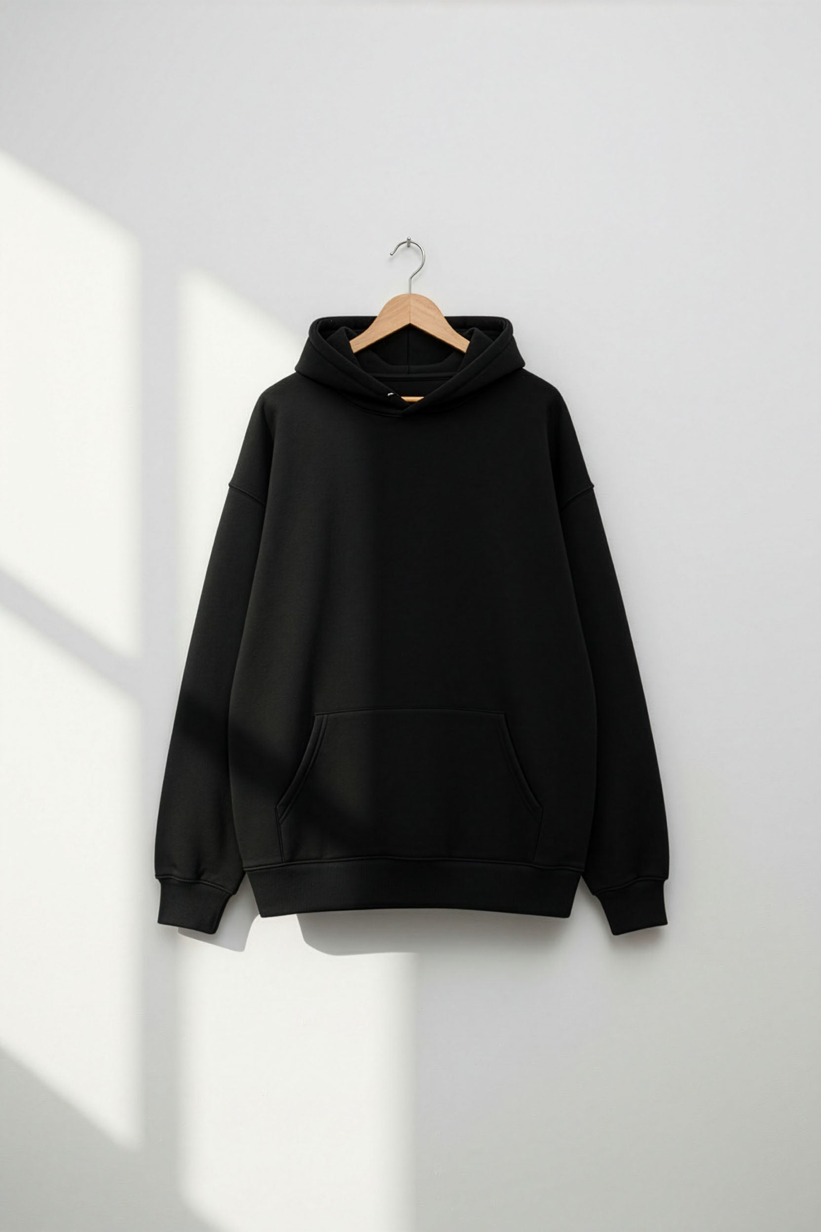 Black hoodie on a hanger against a white wall with sunlight casting shadows.