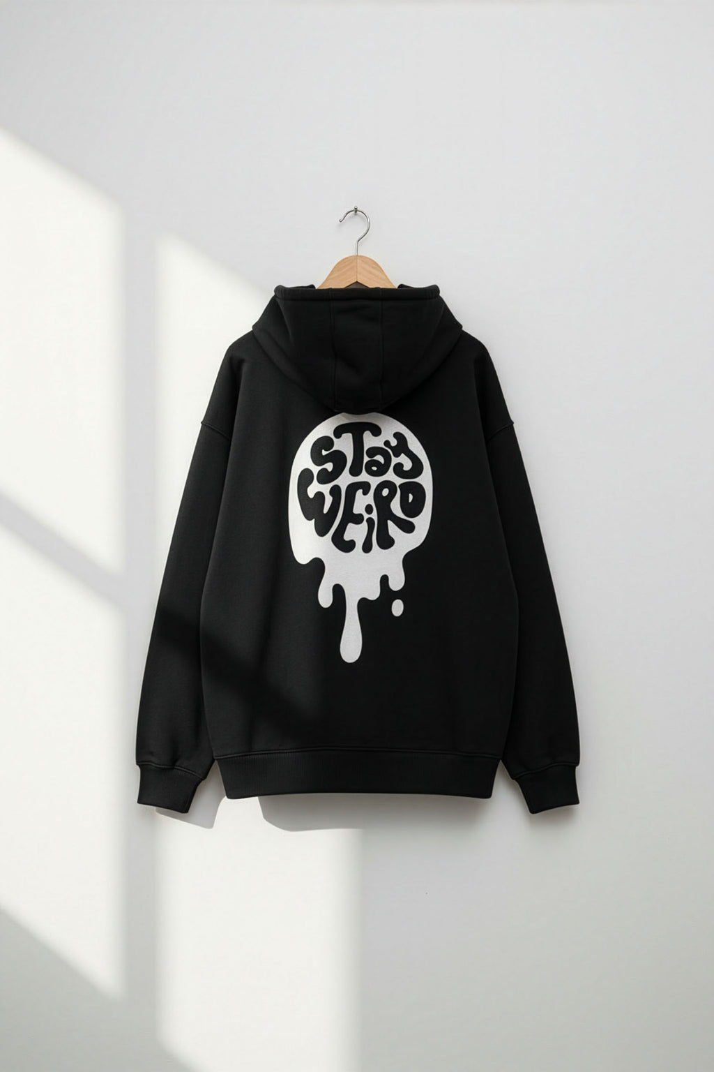 Black hoodie with a white graphic design on the back, hanging against a white wall.