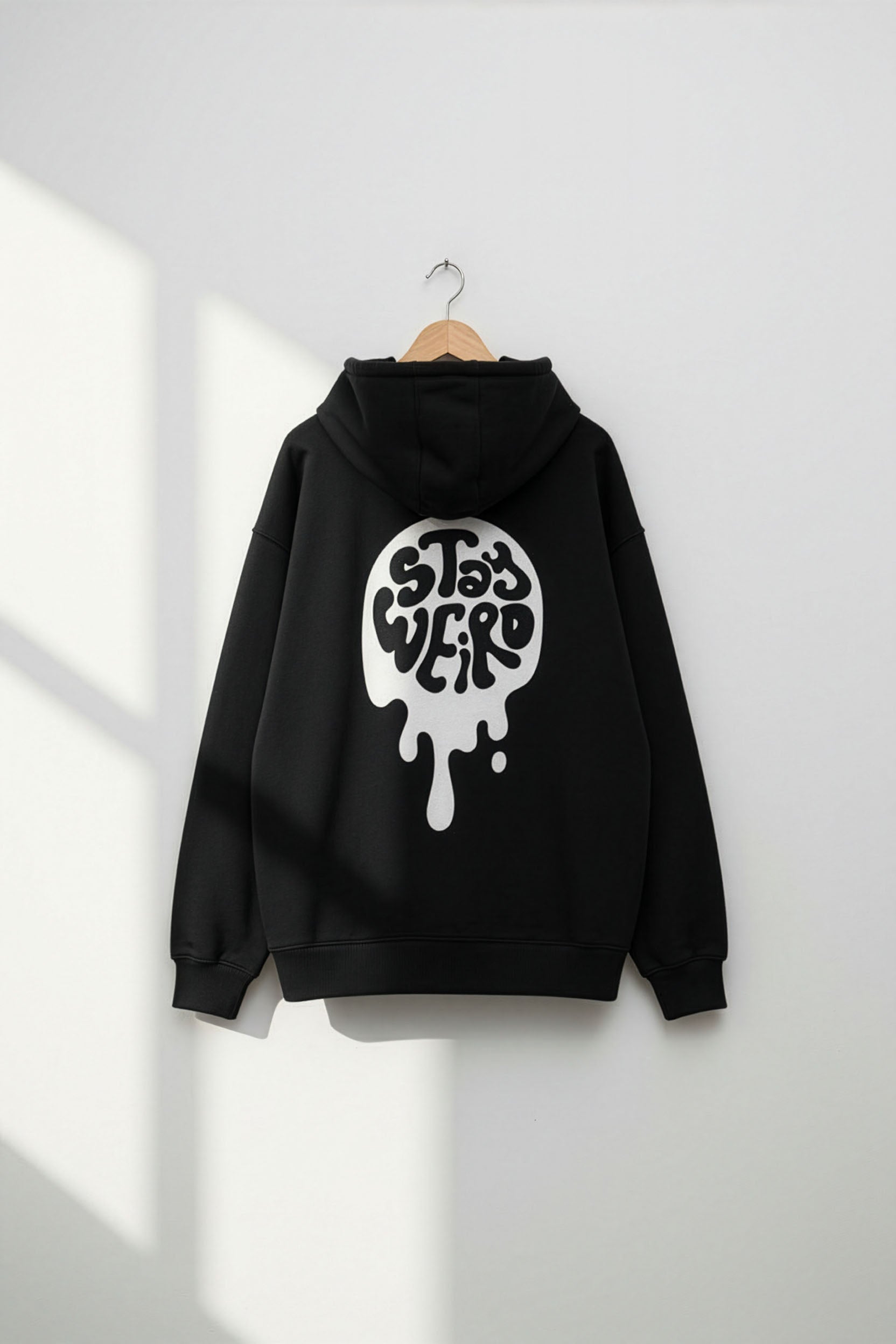 Black hoodie with a white graphic design on the back, hanging against a white wall.