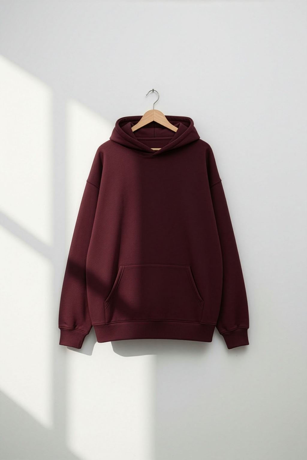 Maroon hoodie on a hanger against a white wall