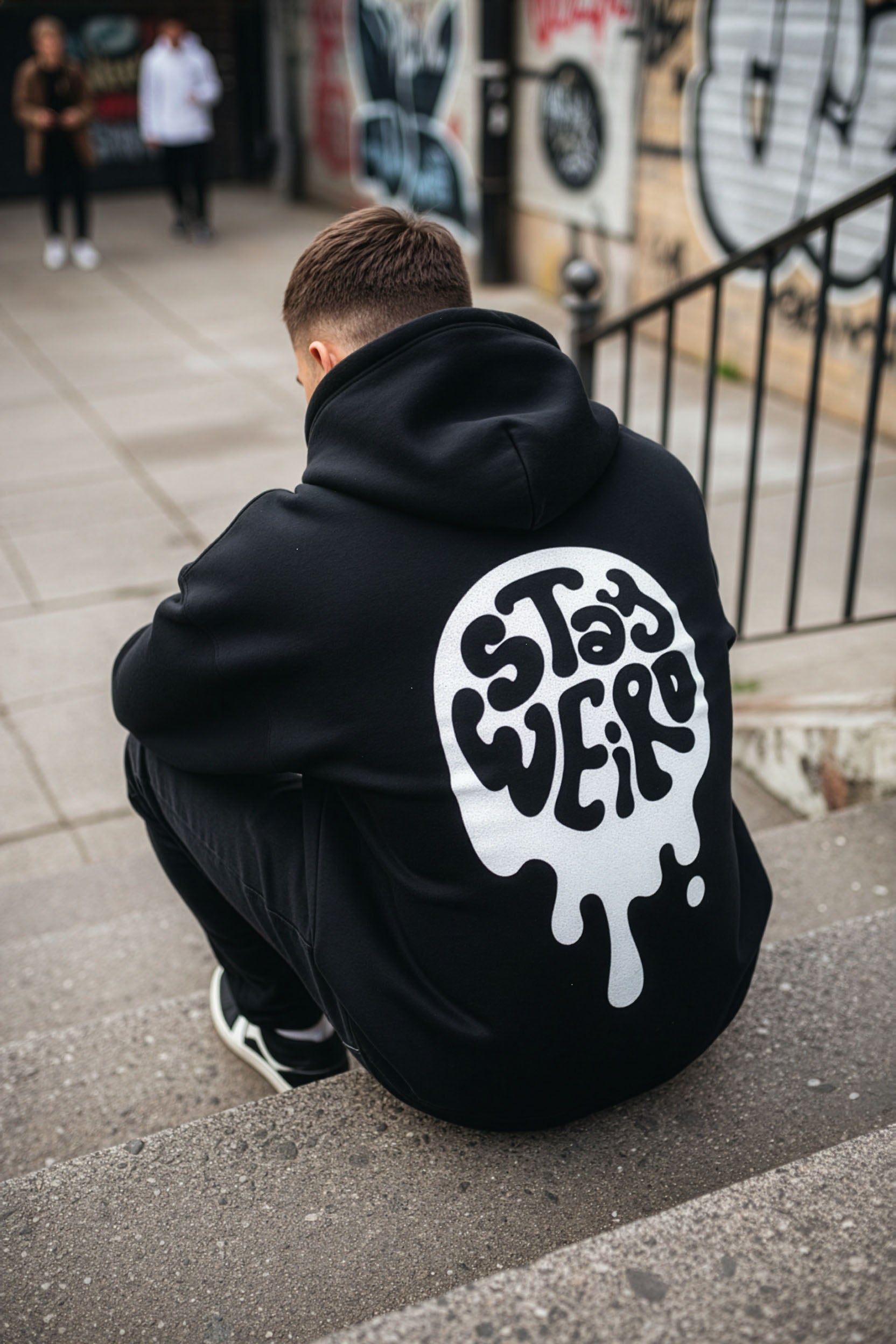 Person wearing a black hoodie with a white graphic design sitting on a street.