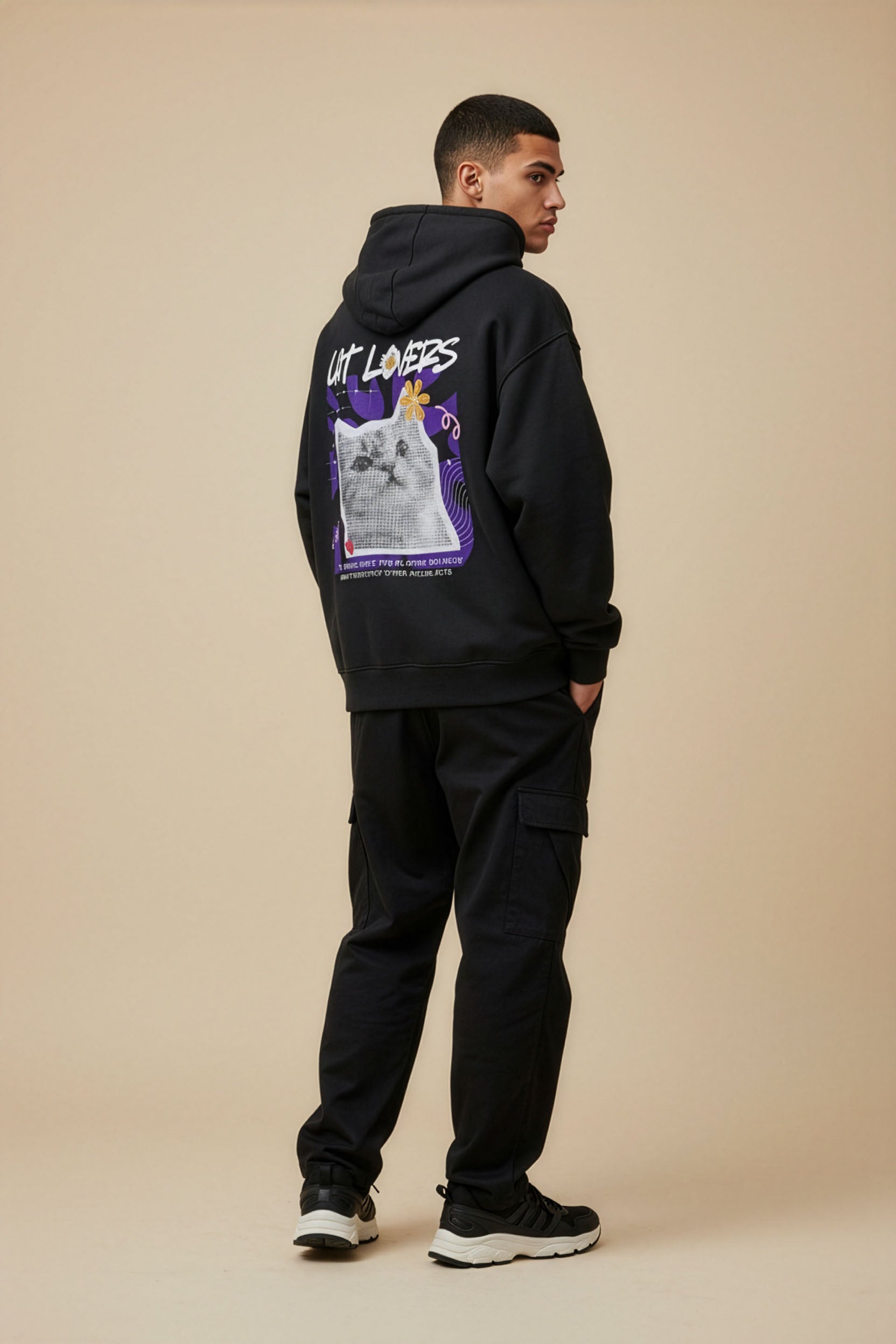 Person wearing a black hoodie with graphic design on the back against a beige background