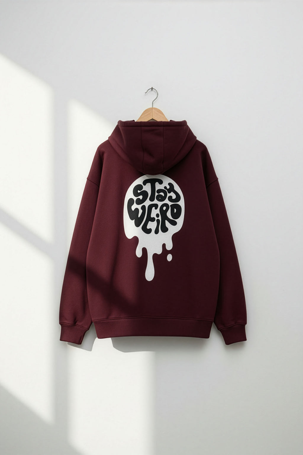 Maroon hoodie with a white graphic on the back, hanging against a white wall.