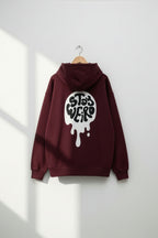 Maroon hoodie with a white graphic on the back, hanging against a white wall.