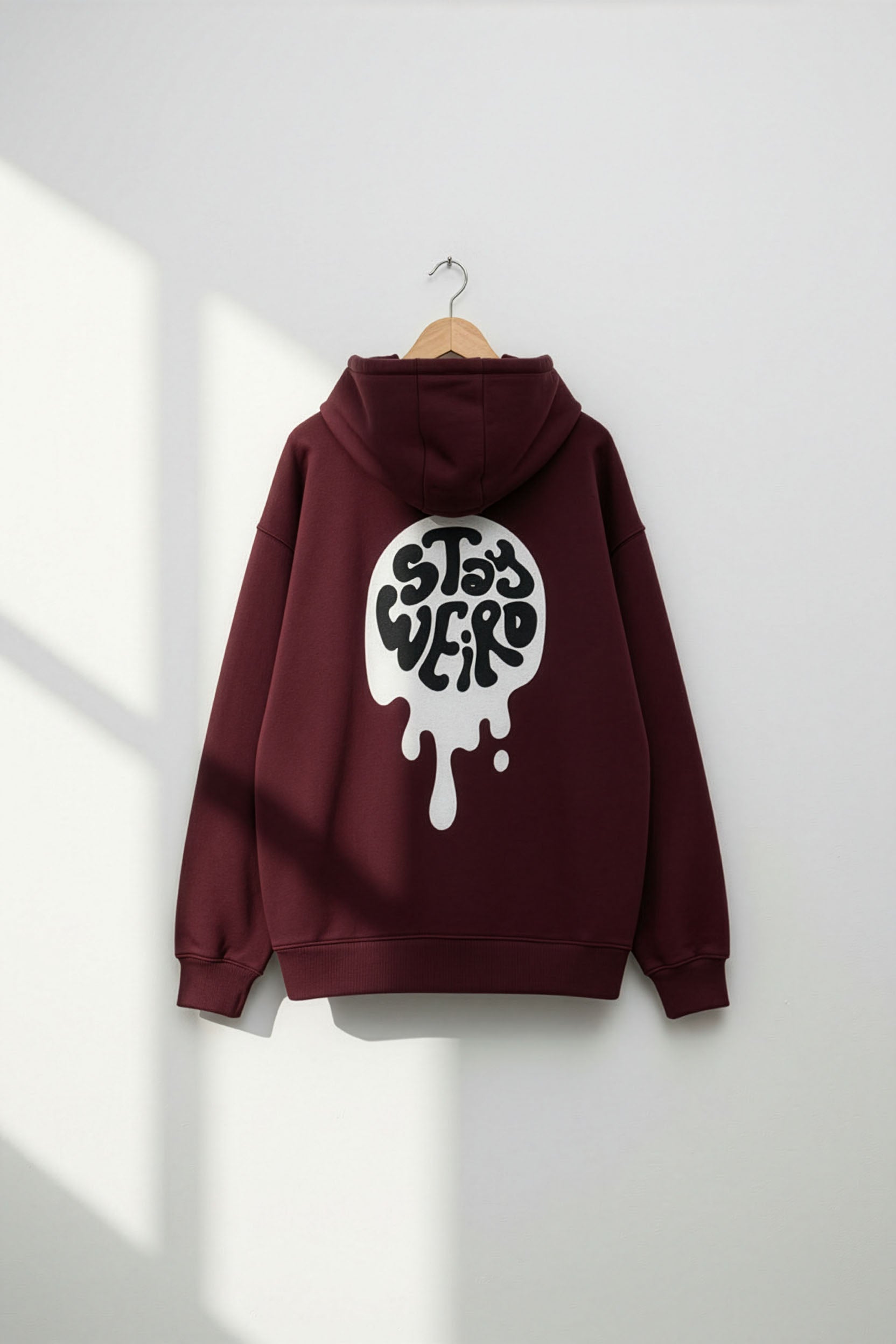 Maroon hoodie with a white graphic on the back, hanging against a white wall.