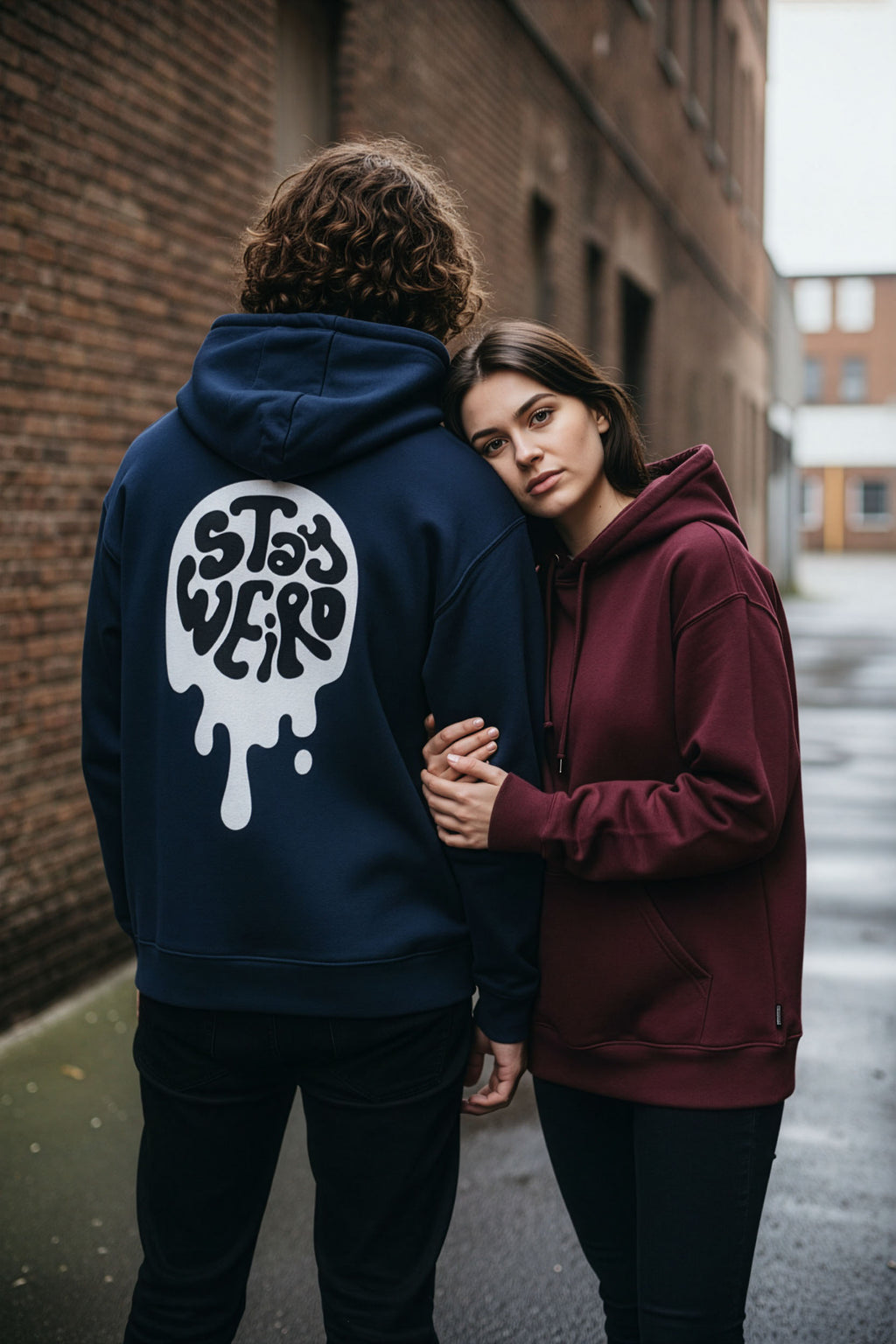 Two people wearing hoodies, one with a visible brand logo, standing close together on a street.
