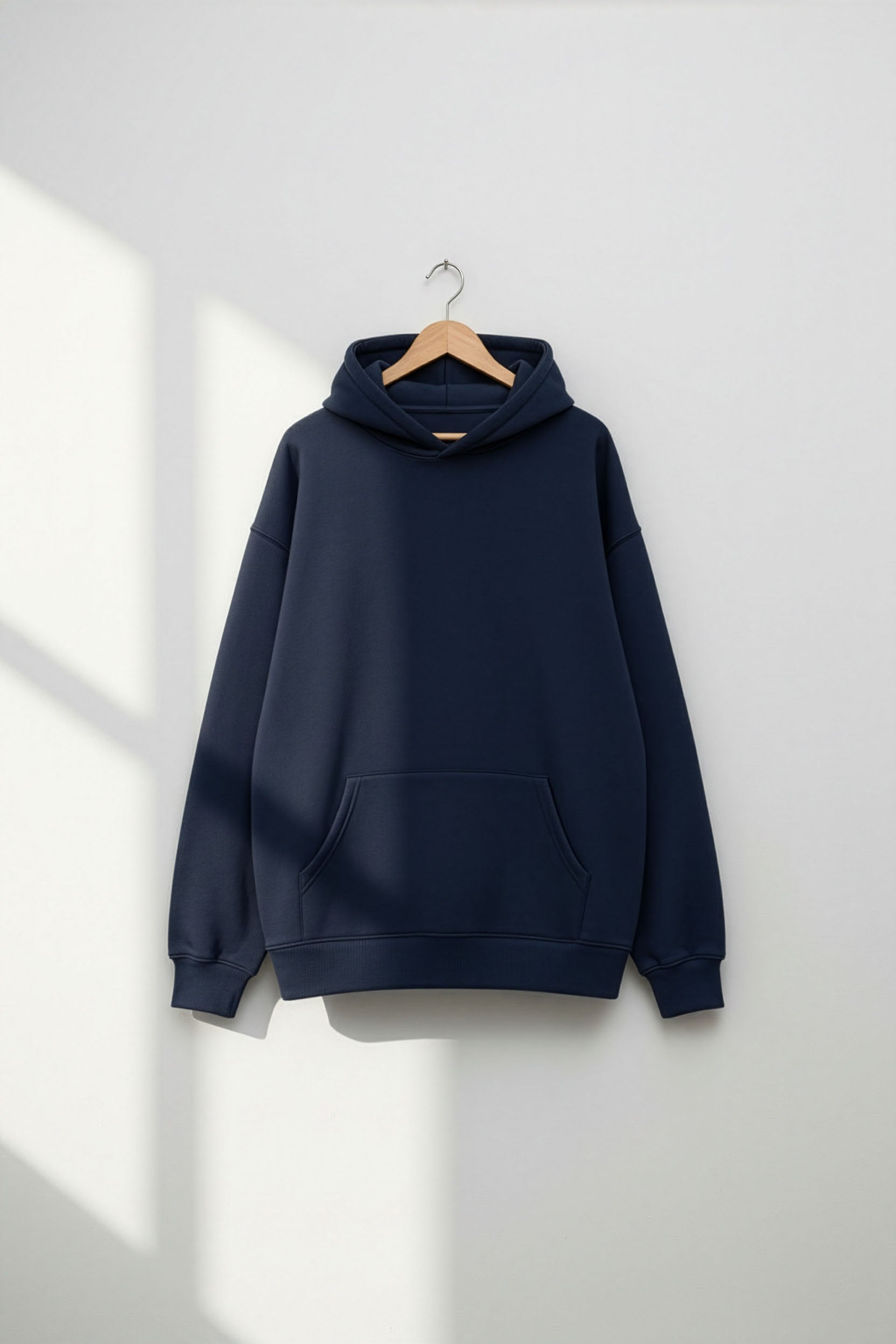 Navy blue hoodie on a wooden hanger against a white wall
